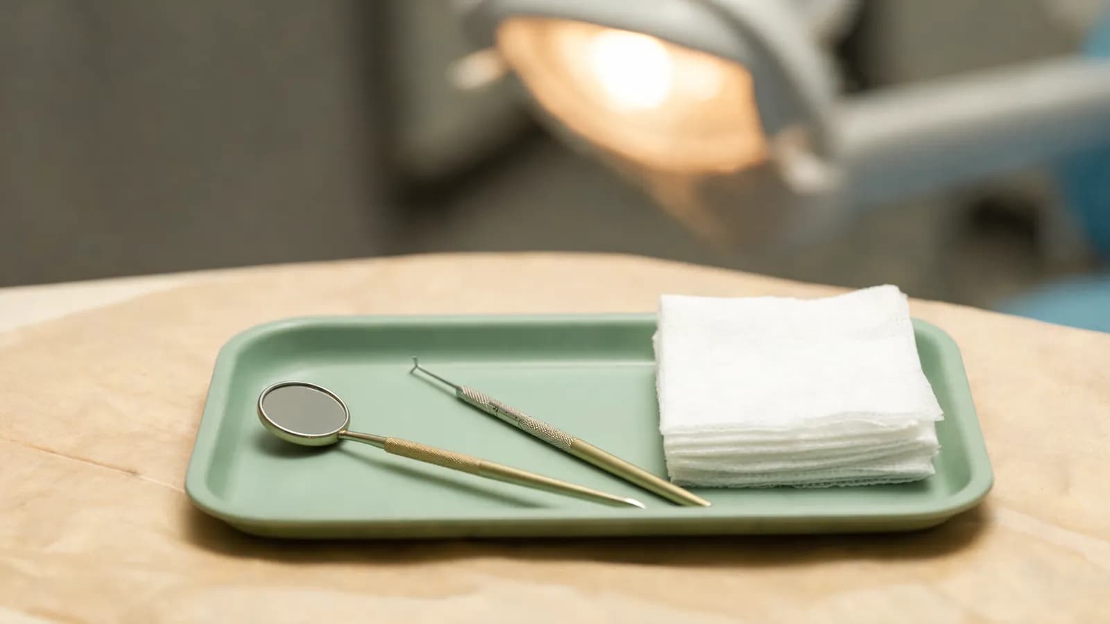 A dental mouth mirror, periodontal probe and sterile gauze on a clean examination tray